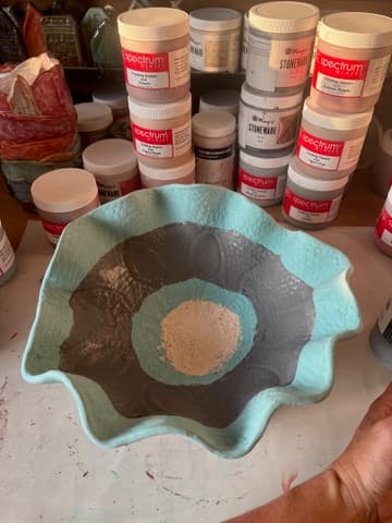 Glazed bowl in turquoise and grey on the workbench, among the glaze jars